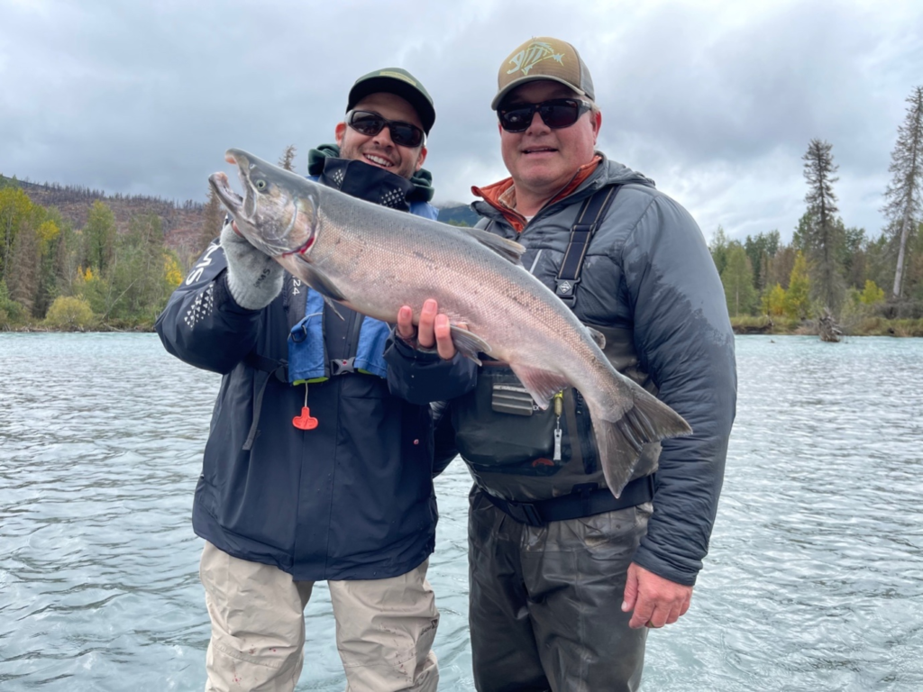 an angler holding silver salmon as his fishing guide looks on