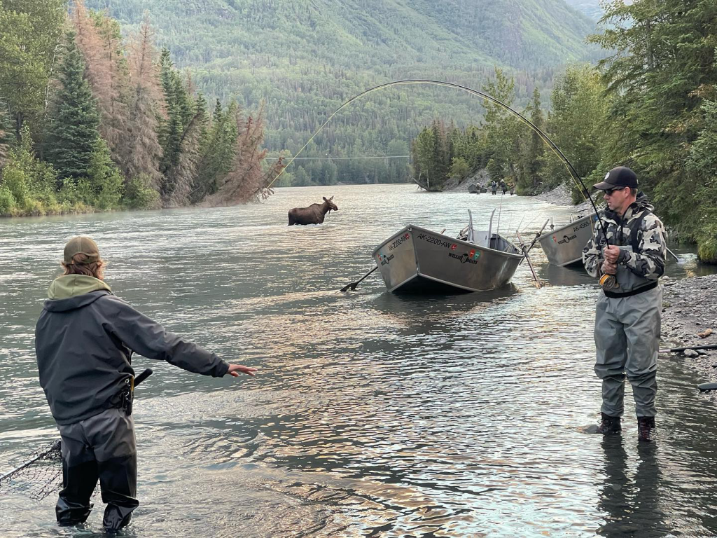 A family fishing in the Kenai River with scenic views in the background.