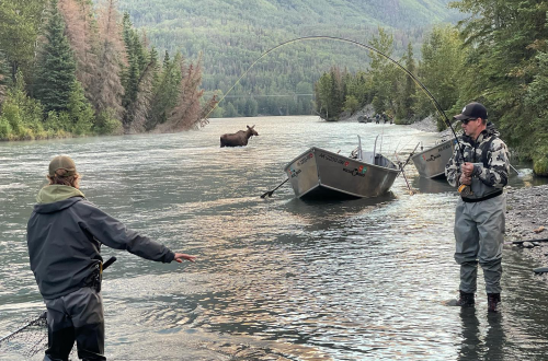 A family fishing in the Kenai River with scenic views in the background.