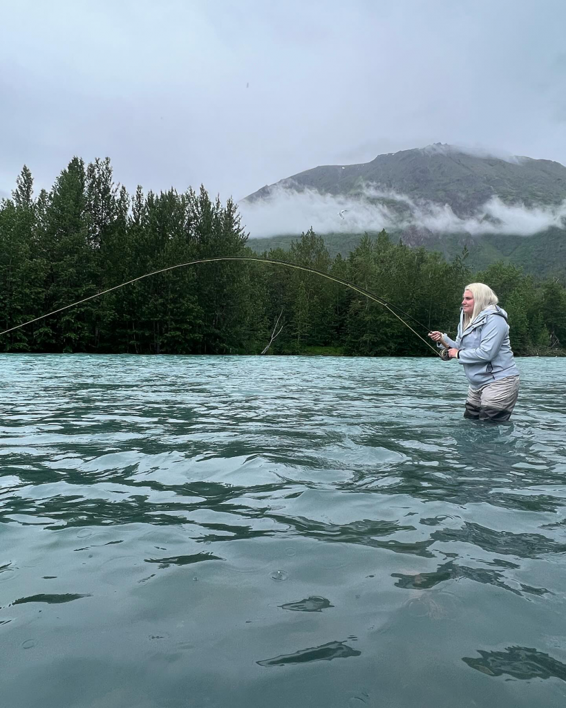 A person casts a fishing line into the flowing waters of the Kenai River, demonstrating the commitment to sustainable fishing