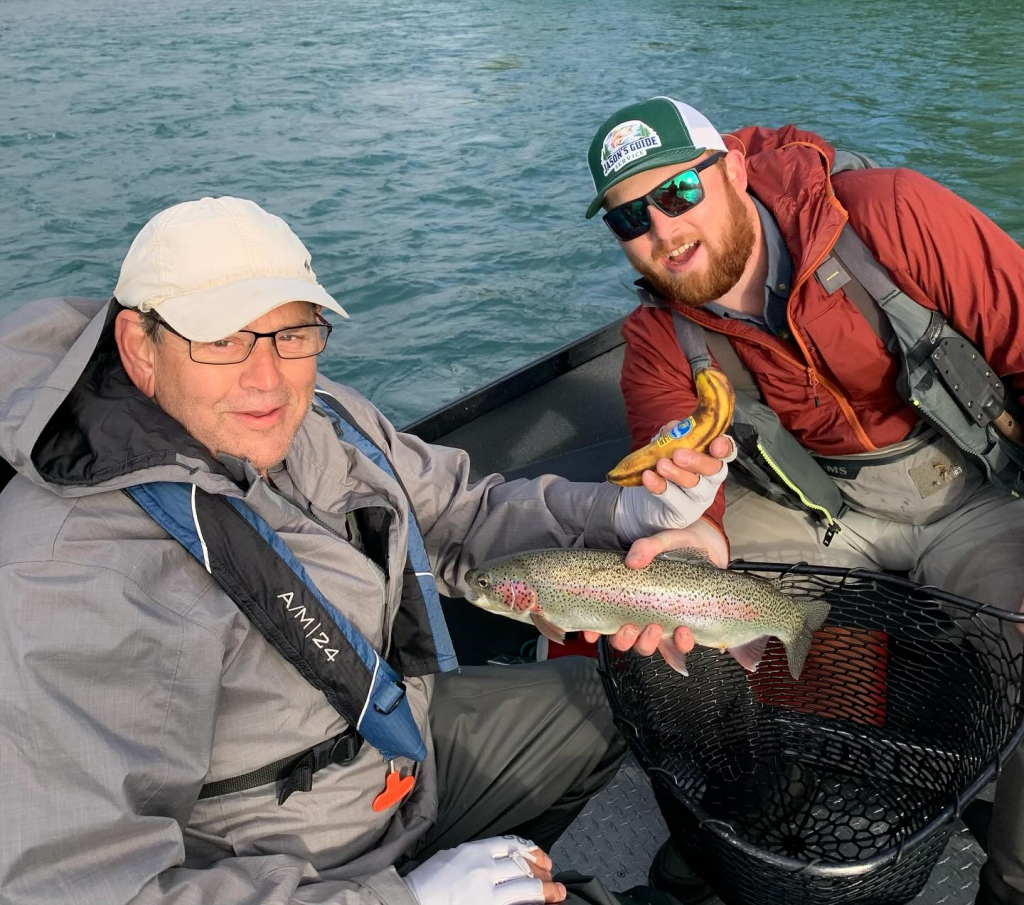 Two anglers are on a boat, showing the rainbow trout they just caught