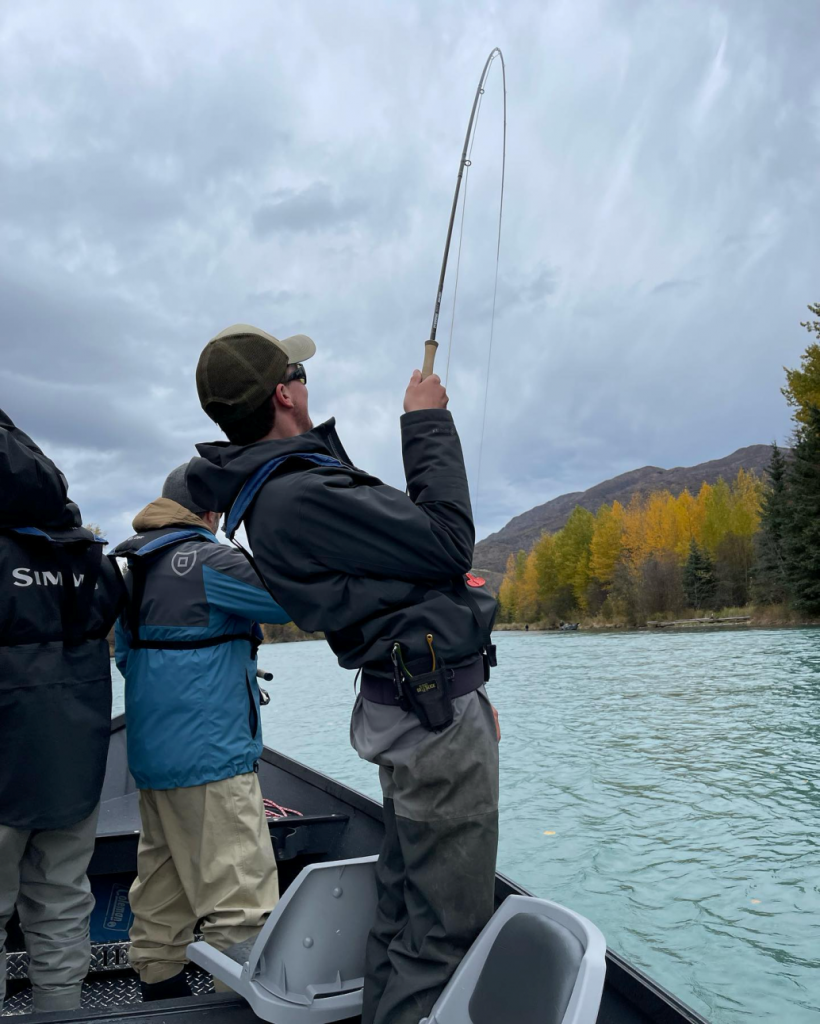 An angler reeling in a catch while wearing waterproof clothing on the Kenai River.