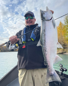 An angler holding a big silver salmon on a drift boat on the Kenai River.