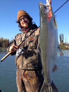 An angler proudly holding a silver salmon by the Kenai River.