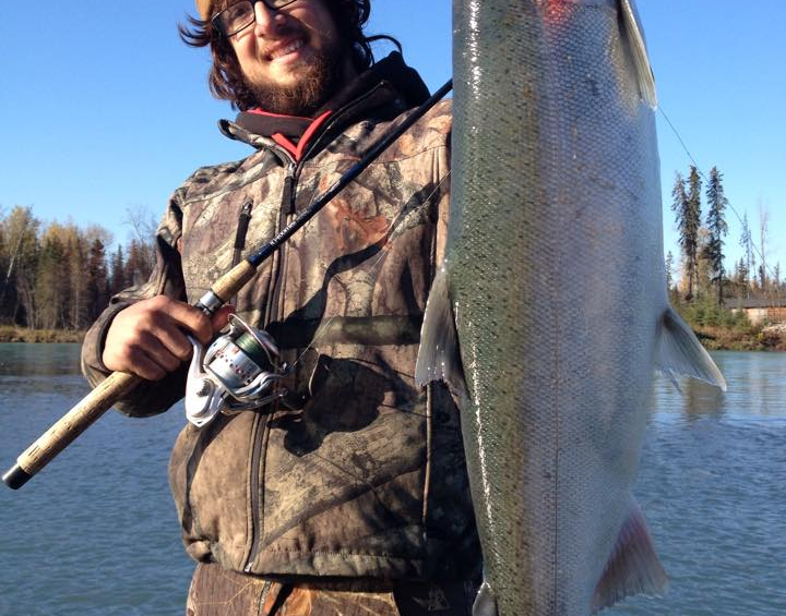 An angler proudly holding a silver salmon by the Kenai River.