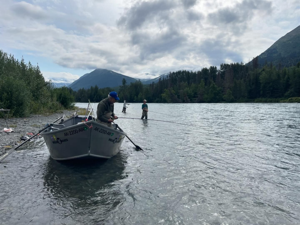 A drift boat with an angler floats on the Kenai River, surrounded by stunning natural scenery.