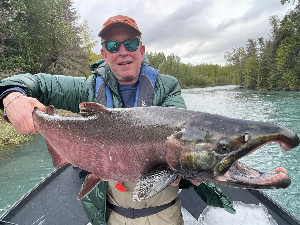 An angler holding a silver salmon in a drift boat on the Kenai River.