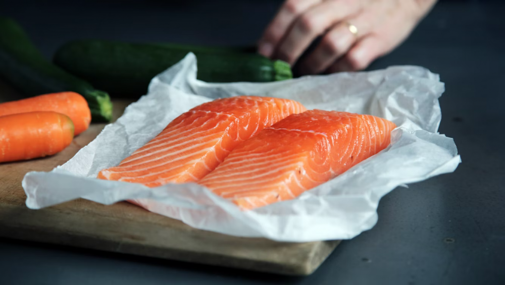 Salmon fillets wrapped in parchment paper on a cutting board.