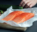 Salmon fillets wrapped in parchment paper on a cutting board.